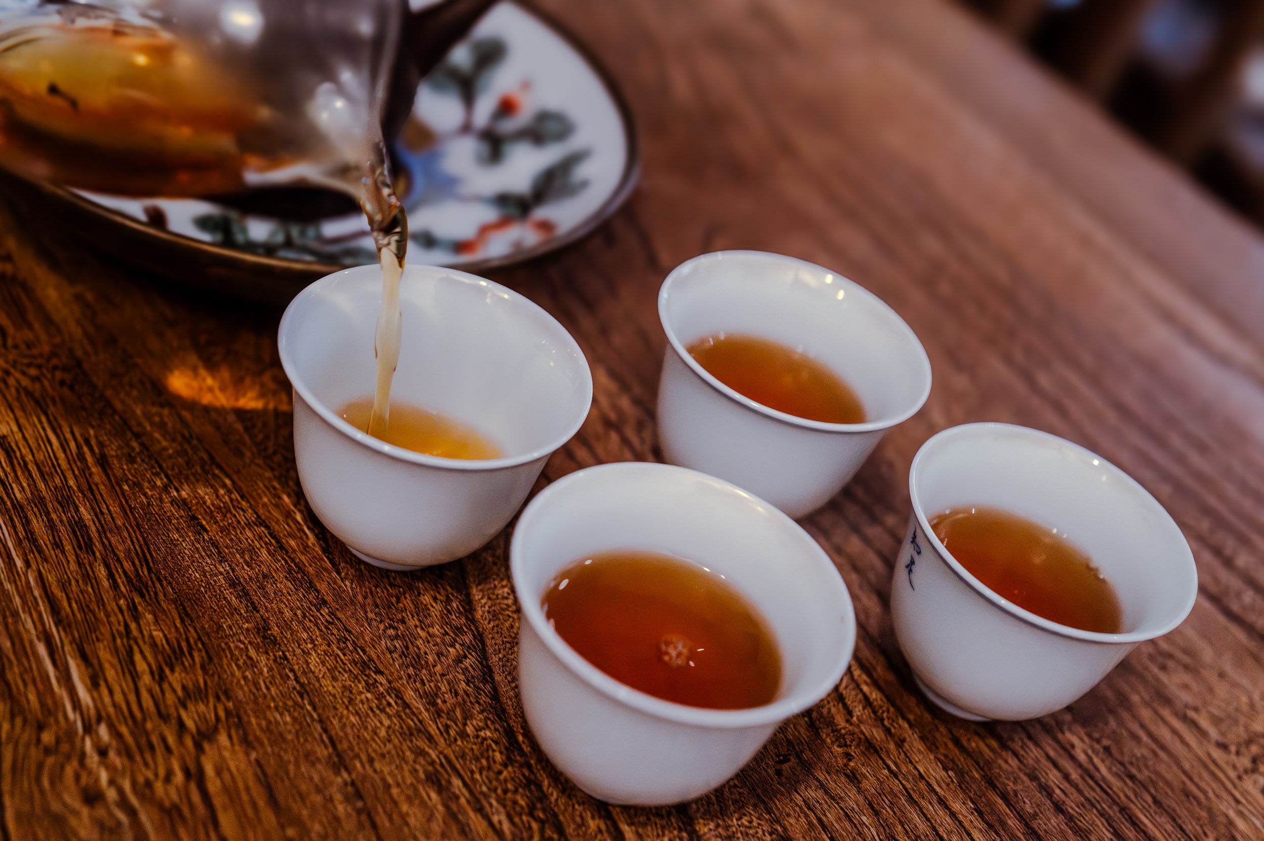 Le thé versé de la théière dans quatre petites tasses de porcelaine blanche, lors d'une dégustation à la boutique