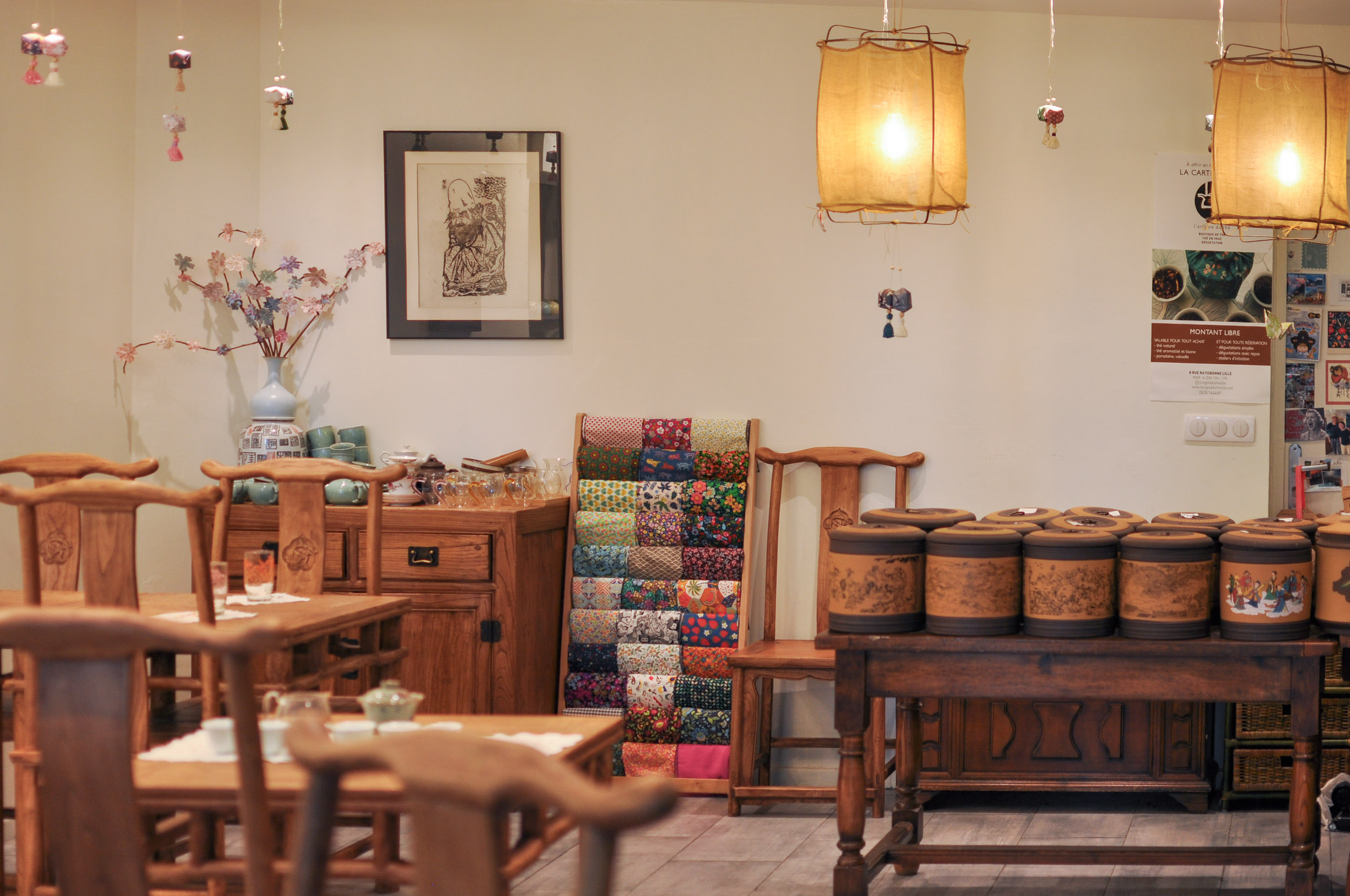 L'intérieur de la boutique : tables et chaises en bois, jarres à thé et lanternes en tissu