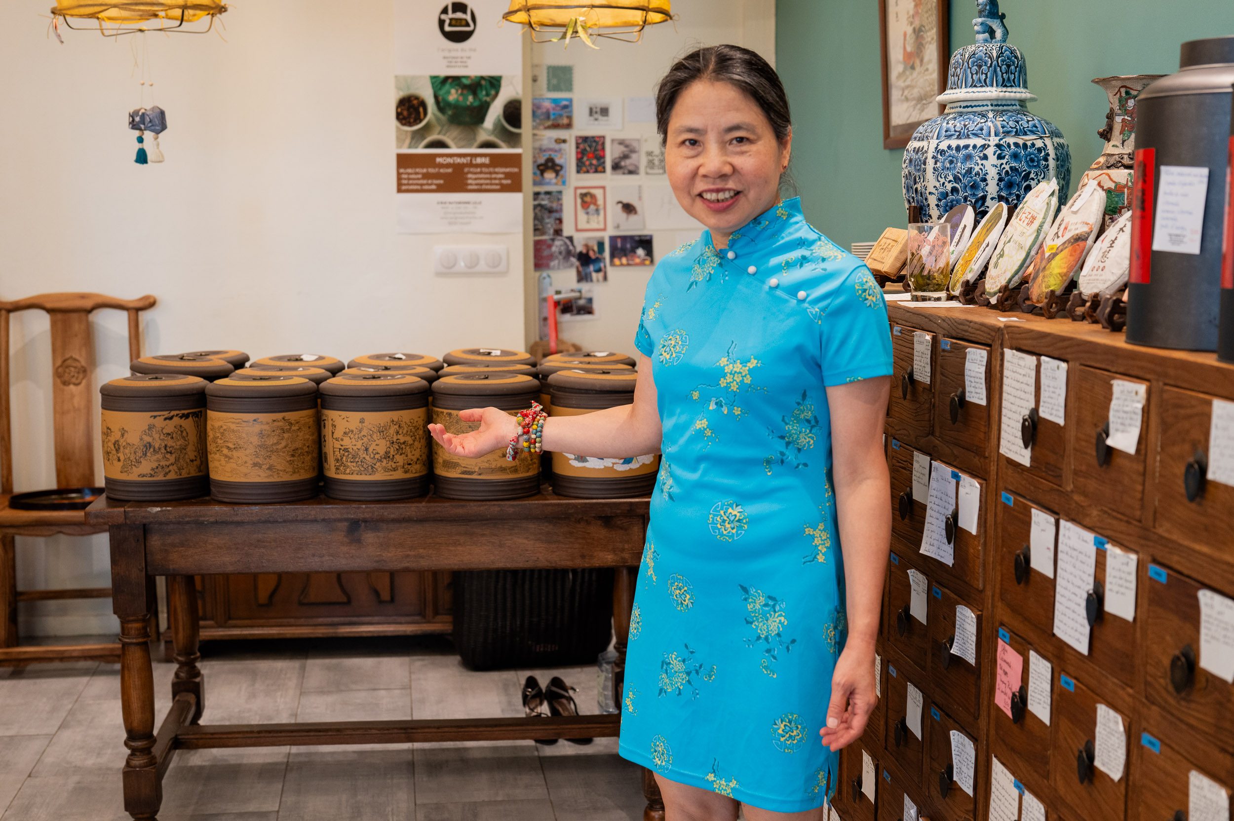 Lijun, souriante, présentant ses jarres de thé et ses tiroirs à thé dans la boutique L'origine du thé