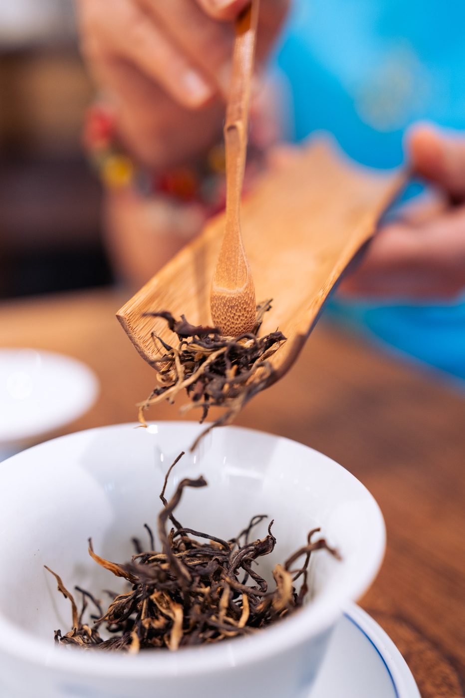 Une main dose les feuilles de thé rouge dans un gaiwan à l'aide d'une pelle en bambou, lors du service à la boutique