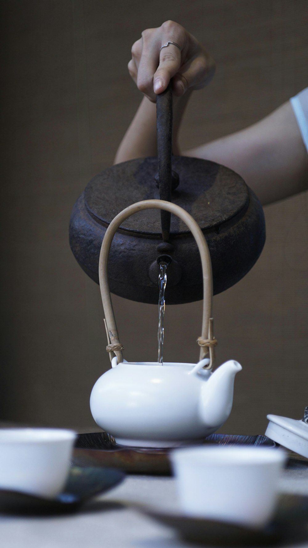 Les mains qui versent l'eau de la bouilloire en fonte dans la théière blanche
